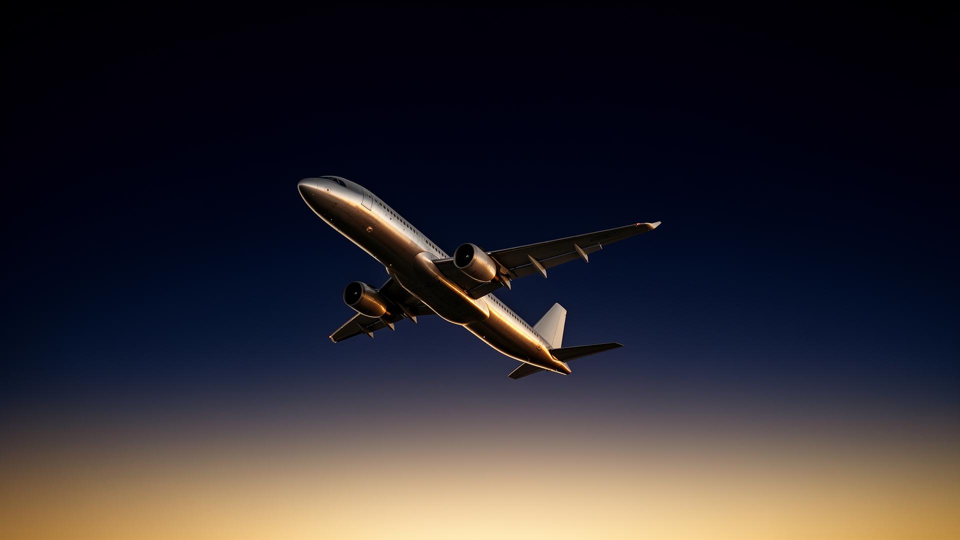 An airliner climbing into a navy and gold sunrise sky